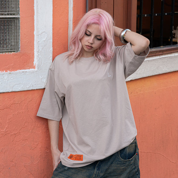 woman with pink hair wearing a beige t-shirt in front of a colorful wall.