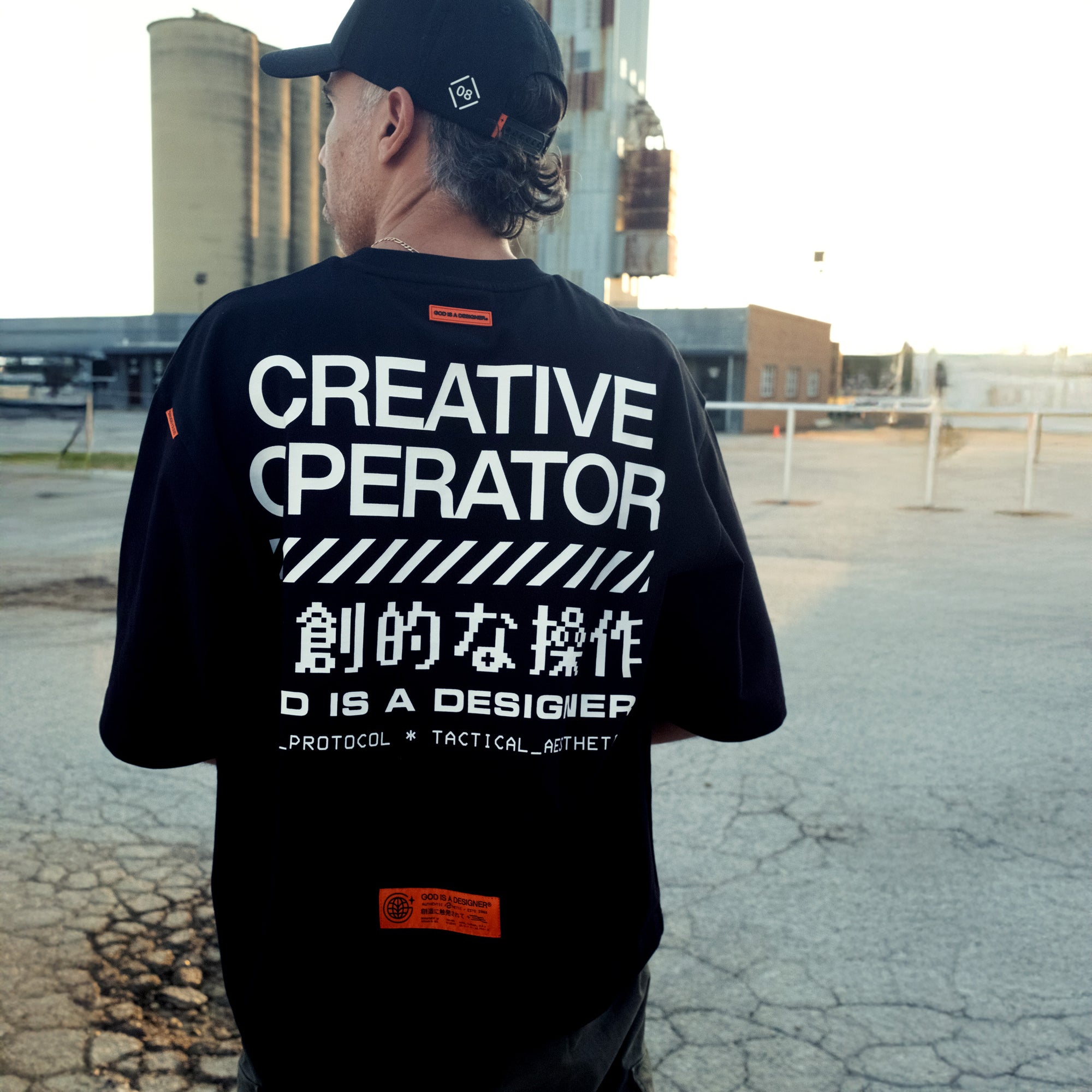 Person wearing a black t-shirt with 'CREATIVE OPERATOR' text outdoors.